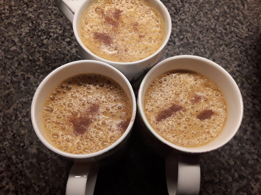Three cups of frothy golden milk or turmeric tea topped with a sprinkle of cinnamon